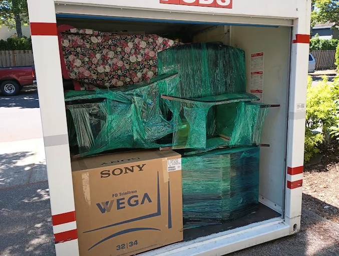 A moving container packed with wrapped furniture, boxes, and a large television box secured inside.